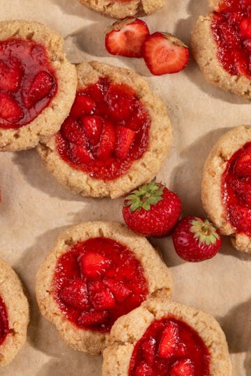 tray of overlapping cookies filled with strawberry jam alongside fresh strawberries.