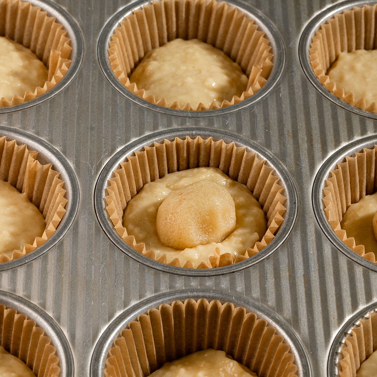 muffin liners ½ filled with batter with ball of almond frangipane in the center.