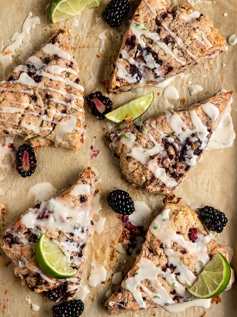 tray with blackberry scones topped with lime slices, icing, and fresh blackberries.