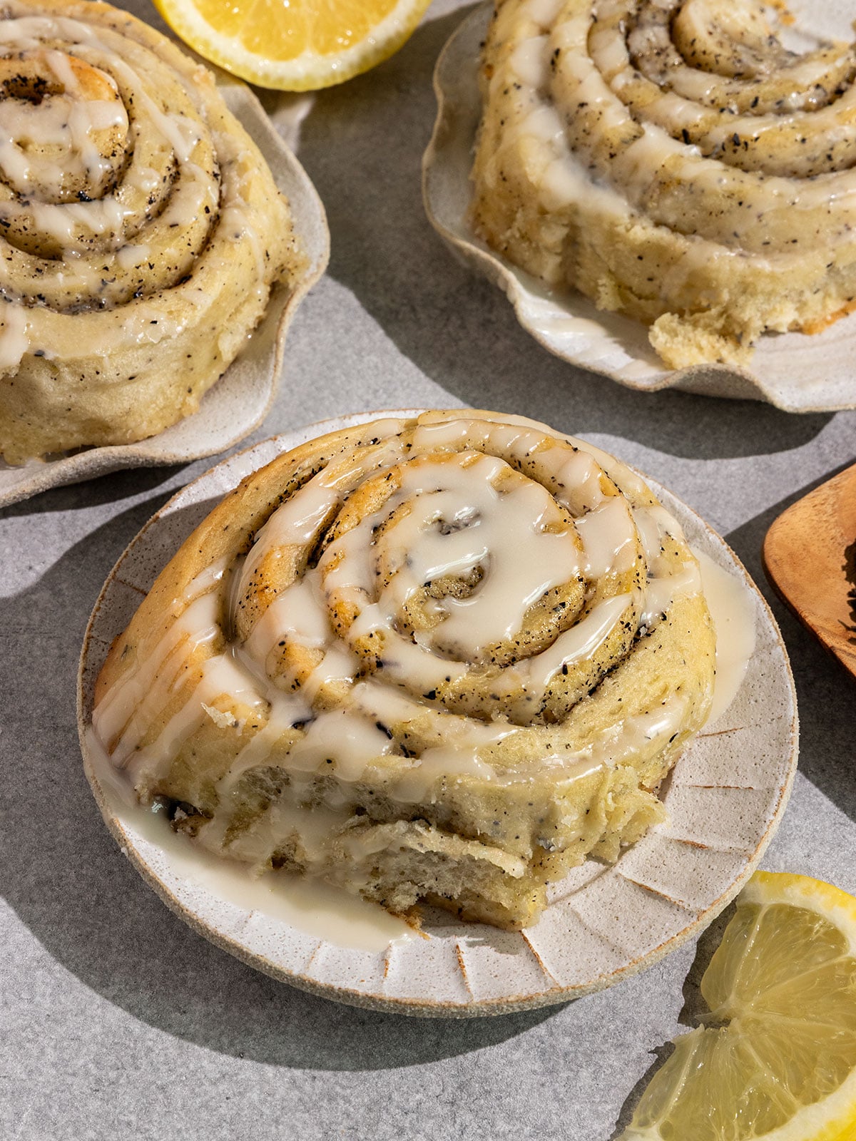 hree sweet rolls on plates filled with swirls of earl grey sugar and topped with a lemon icing with lemon slices on side.