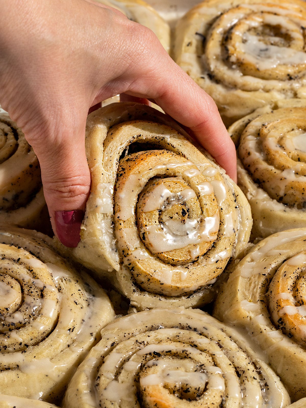 hand pulling out cinnamon roll filled with swirls of earl grey sugar and topped with a lemon icing.