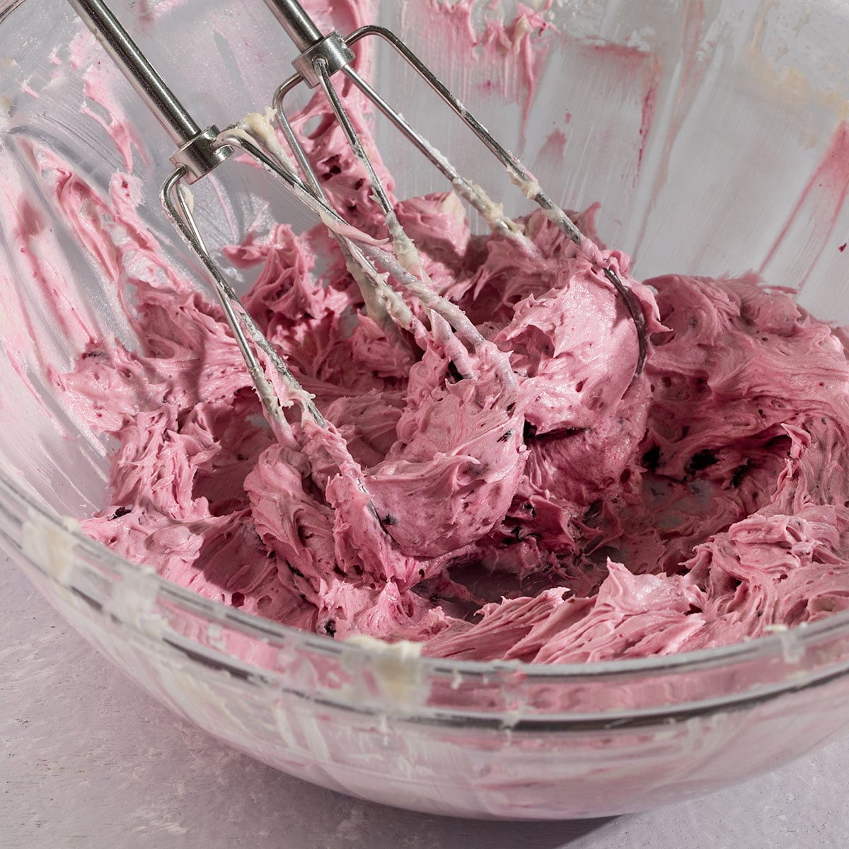 bowl of whipped purple blueberry frosting with electric mixer resting inside.