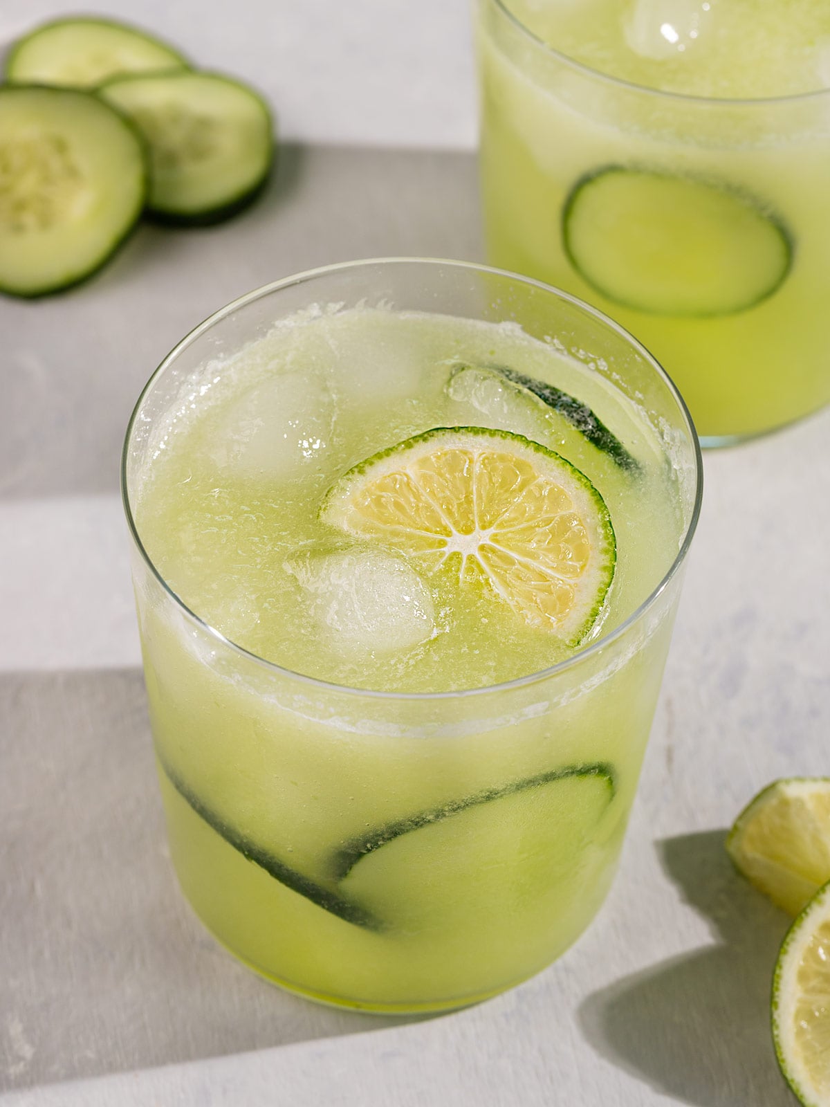 two glasses of green agua fresca juice with cucumber slices and lime wedge.