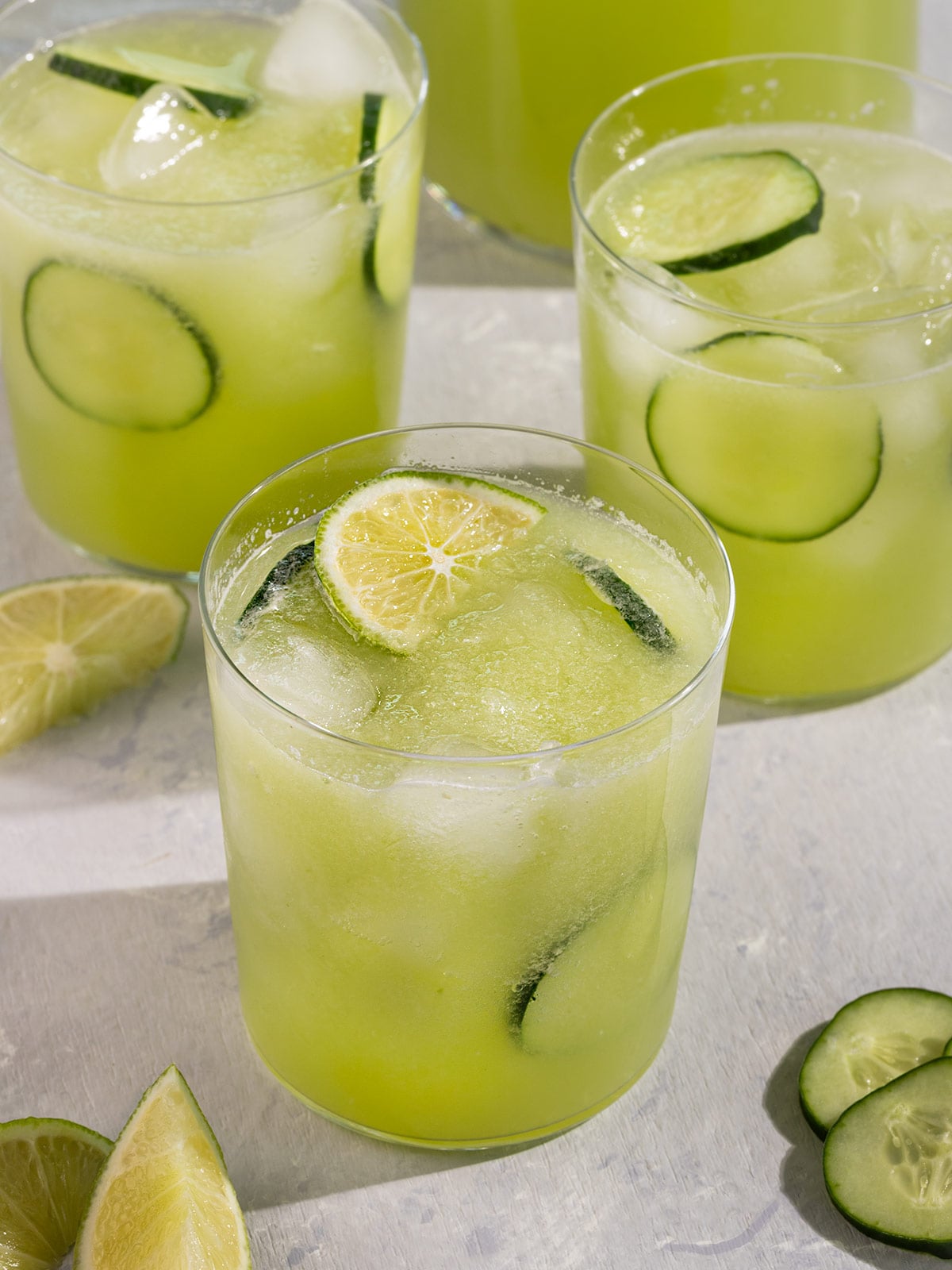 three glasses of green agua fresca juice with cucumber slices and lime wedges