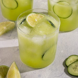 three glasses of green agua fresca juice with cucumber slices and lime wedges.