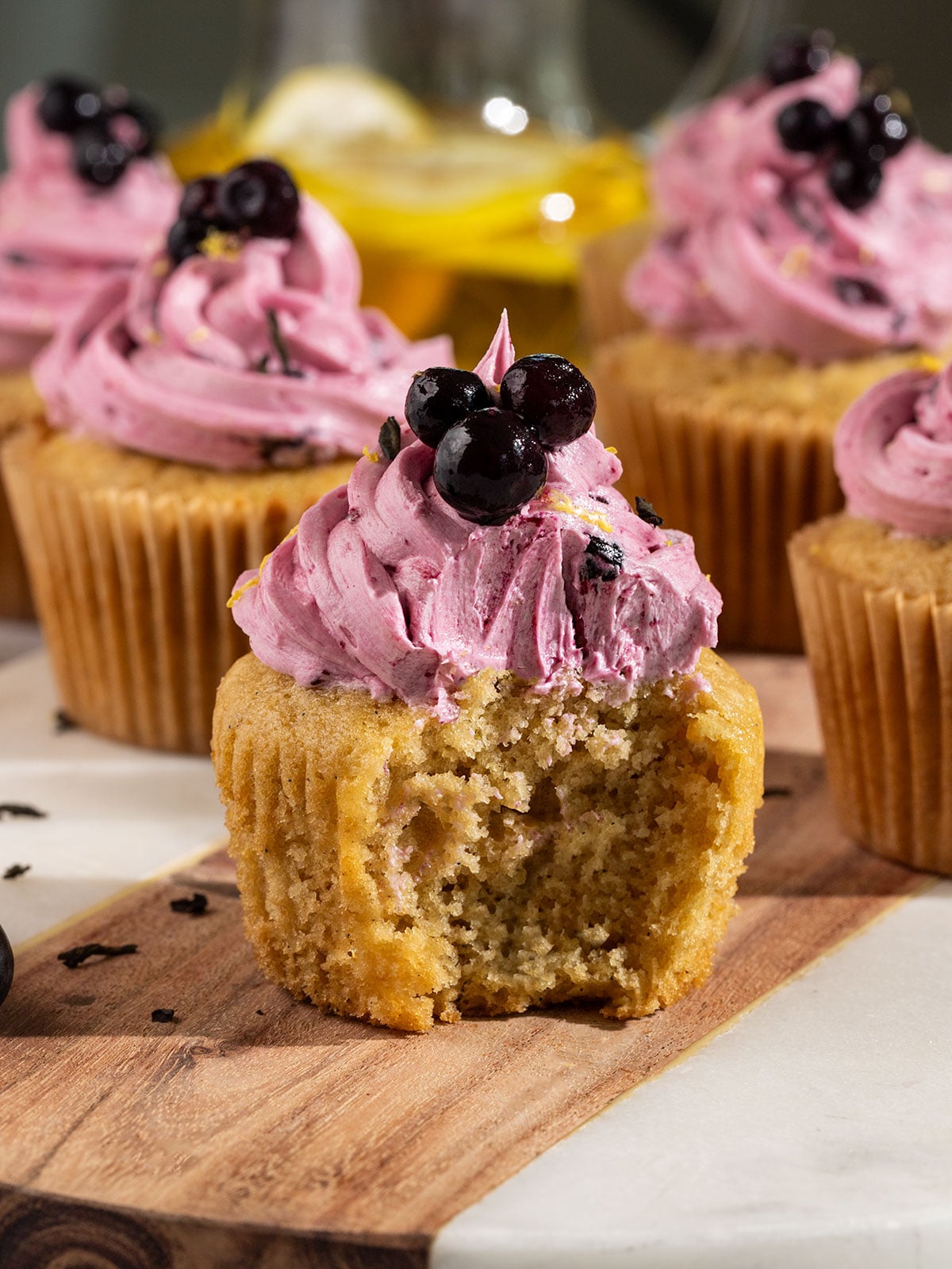 marble board with earl grey cupcakes topped with blueberry frosting with front cupcake having a bite taken out to show inside texture.
