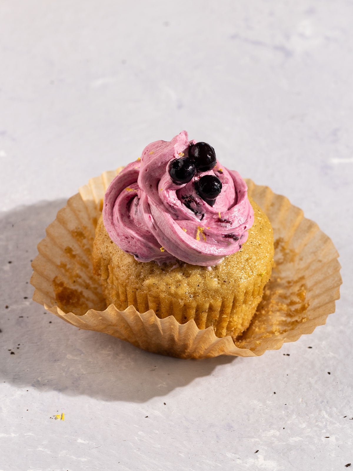 earl grey cupcake inside unwrapped brown cupcake liner with blueberry frosting and fresh blueberries on top.