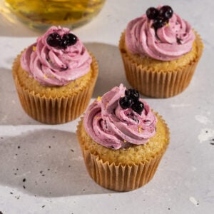 three earl grey cupcakes topped with purple blueberry frosting and fresh blueberries with a pot of earl grey lemon tea.