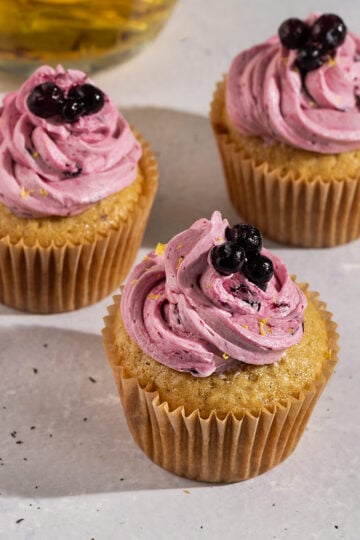 three earl grey cupcakes topped with purple blueberry frosting and fresh blueberries with a pot of earl grey lemon tea.