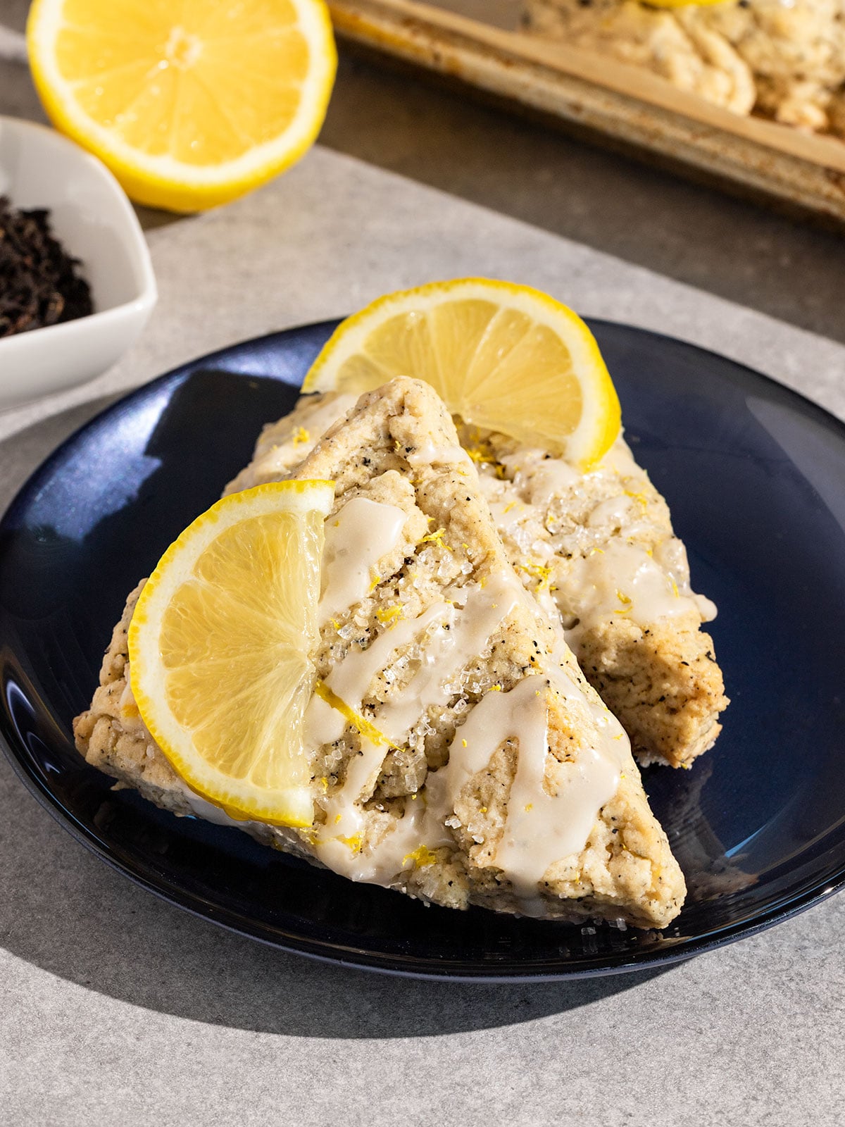 blue plate topped with two earl grey lemon scones with drizzle of lemon icing and lemon slices on top.