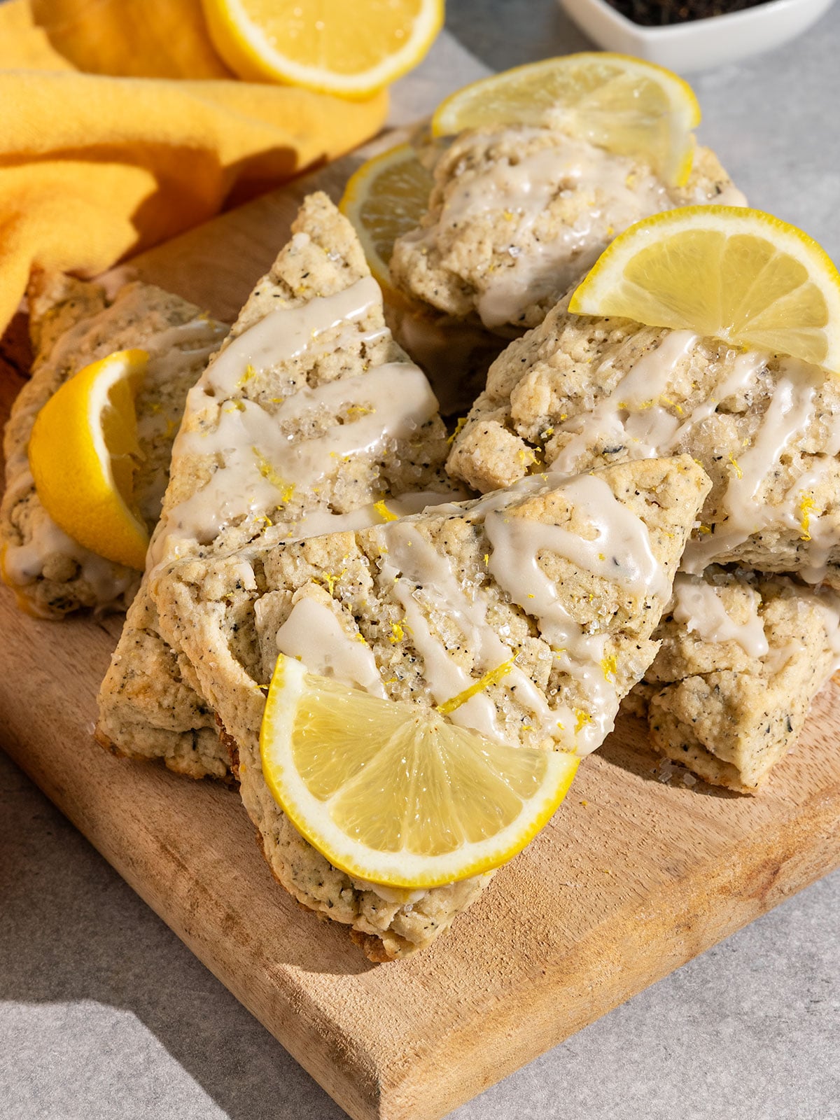 wooden board stacked with lemon earl grey scones topped with drizzle of lemon icing and slices of fresh lemon.