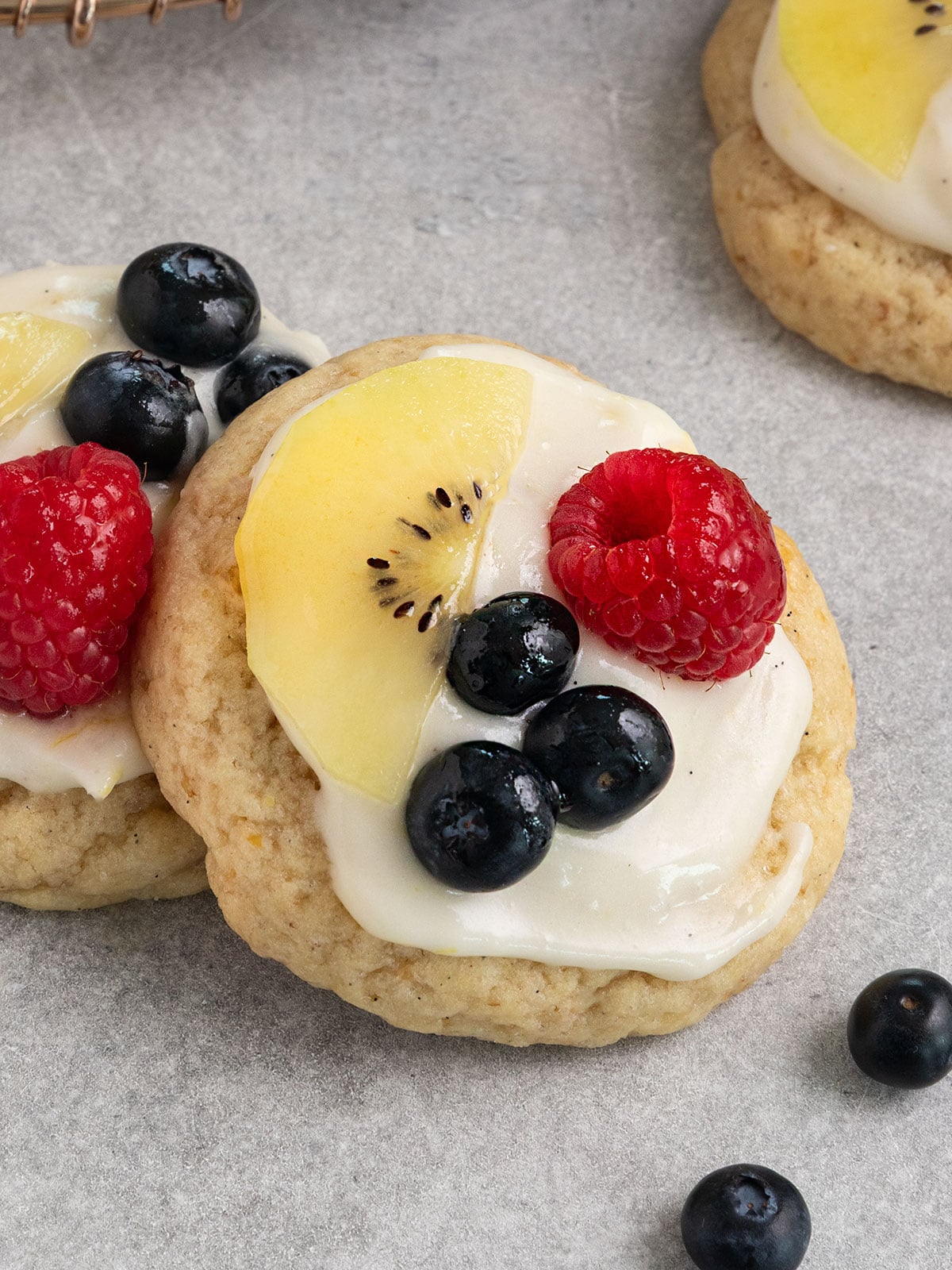 two stacked sugar cookies topped with cream cheese frosting, sliced kiwi, blueberries, and raspberries.