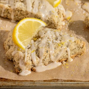 lemon earl grey scone on a parchment lined baking tray topped with lemon icing, lemon zest, and sliced lemon.