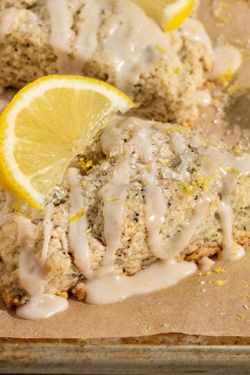 lemon earl grey scone on a parchment lined baking tray topped with lemon icing, lemon zest, and sliced lemon.