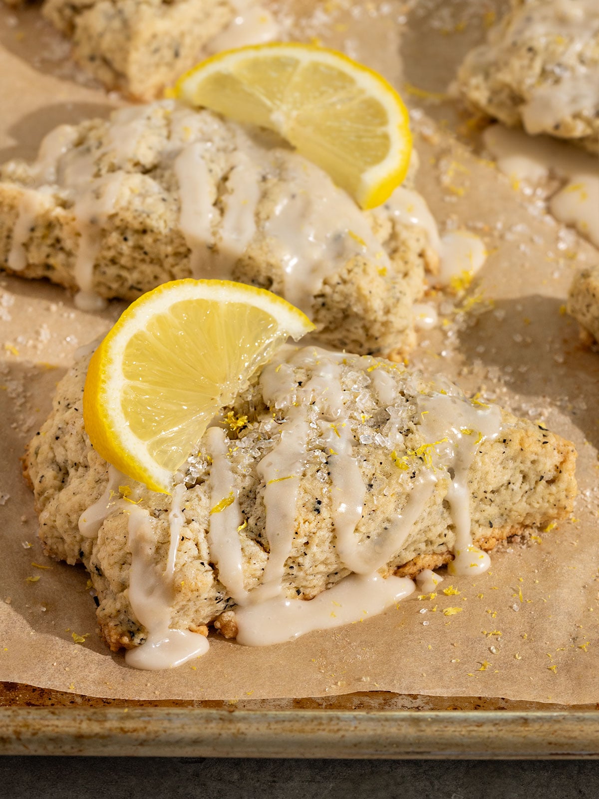 lemon earl grey scone on a parchment lined baking tray topped with lemon icing, lemon zest, and sliced lemon.