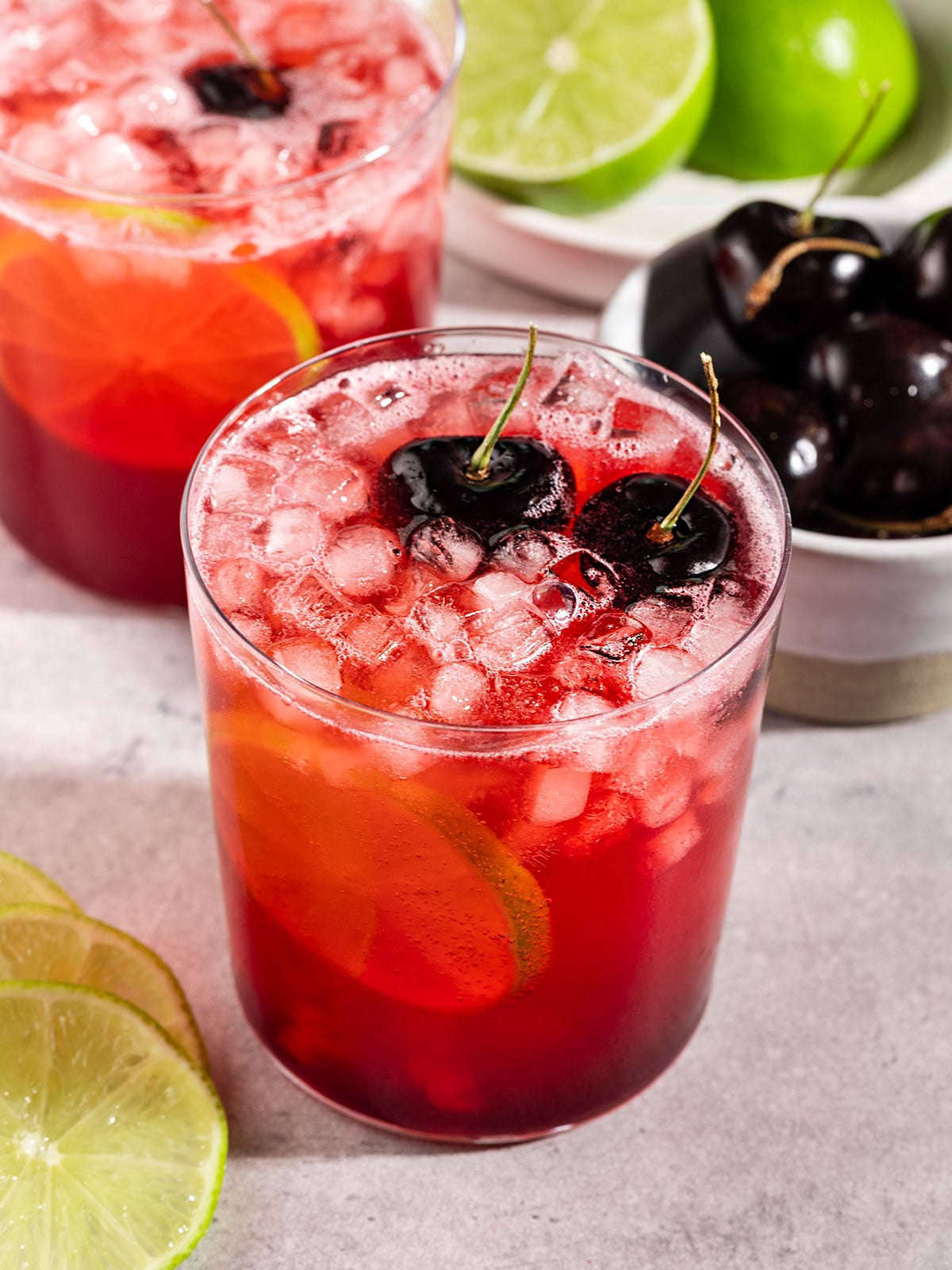 glass of cherry lime soda with ice, fresh cherries, and lime slice.