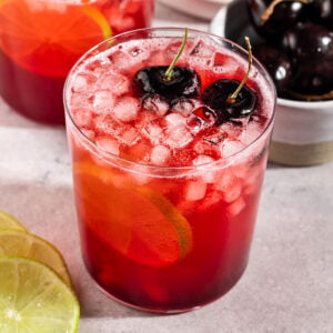 glass of cherry lime soda with ice, fresh cherries, and lime slice.