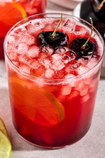 glass of cherry lime soda with ice, fresh cherries, and lime slice.