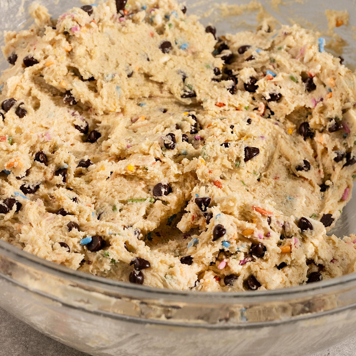 bowl of cookie dough with chocolate chips and rainbow sprinkles mixed in.