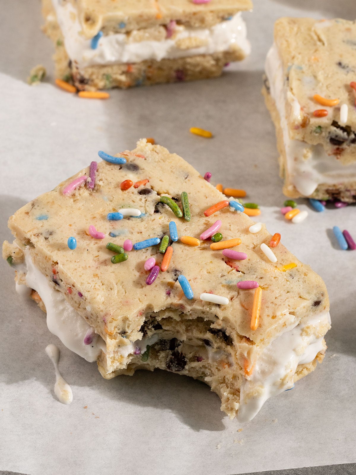 cookie dough ice cream sandwich on parchment paper with a bite taken out.
