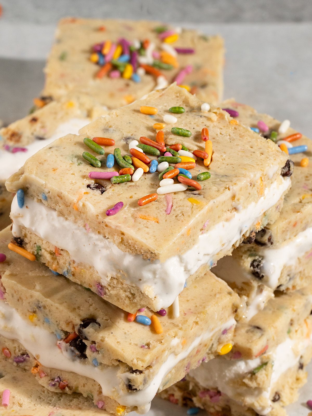 stack of cookie dough ice cream sandwiches filled with vanilla ice cream and topped with rainbow sprinkles.