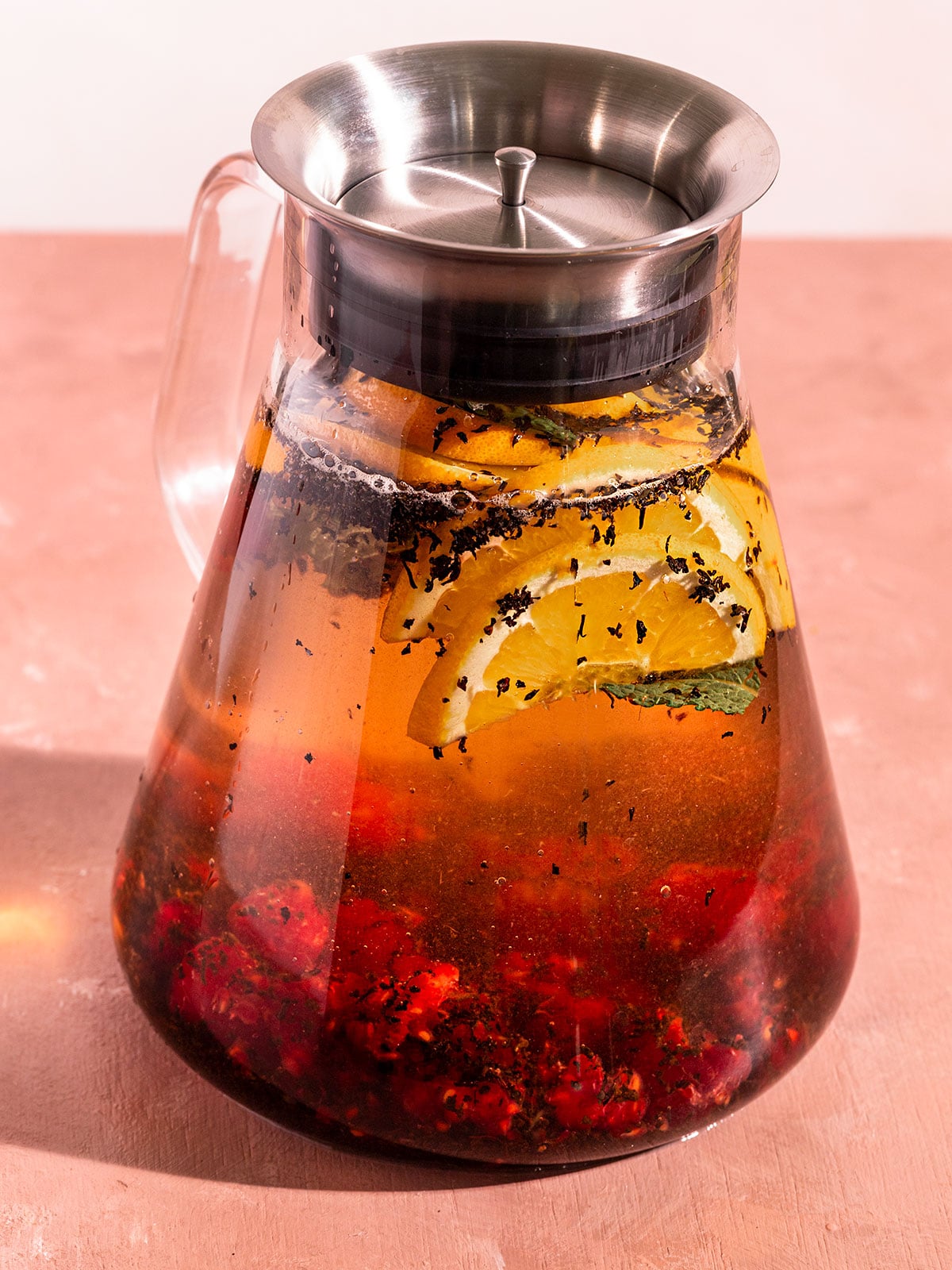 tea pot filled with water, muddled raspberries, black tea leaves, orange slices, and mint.