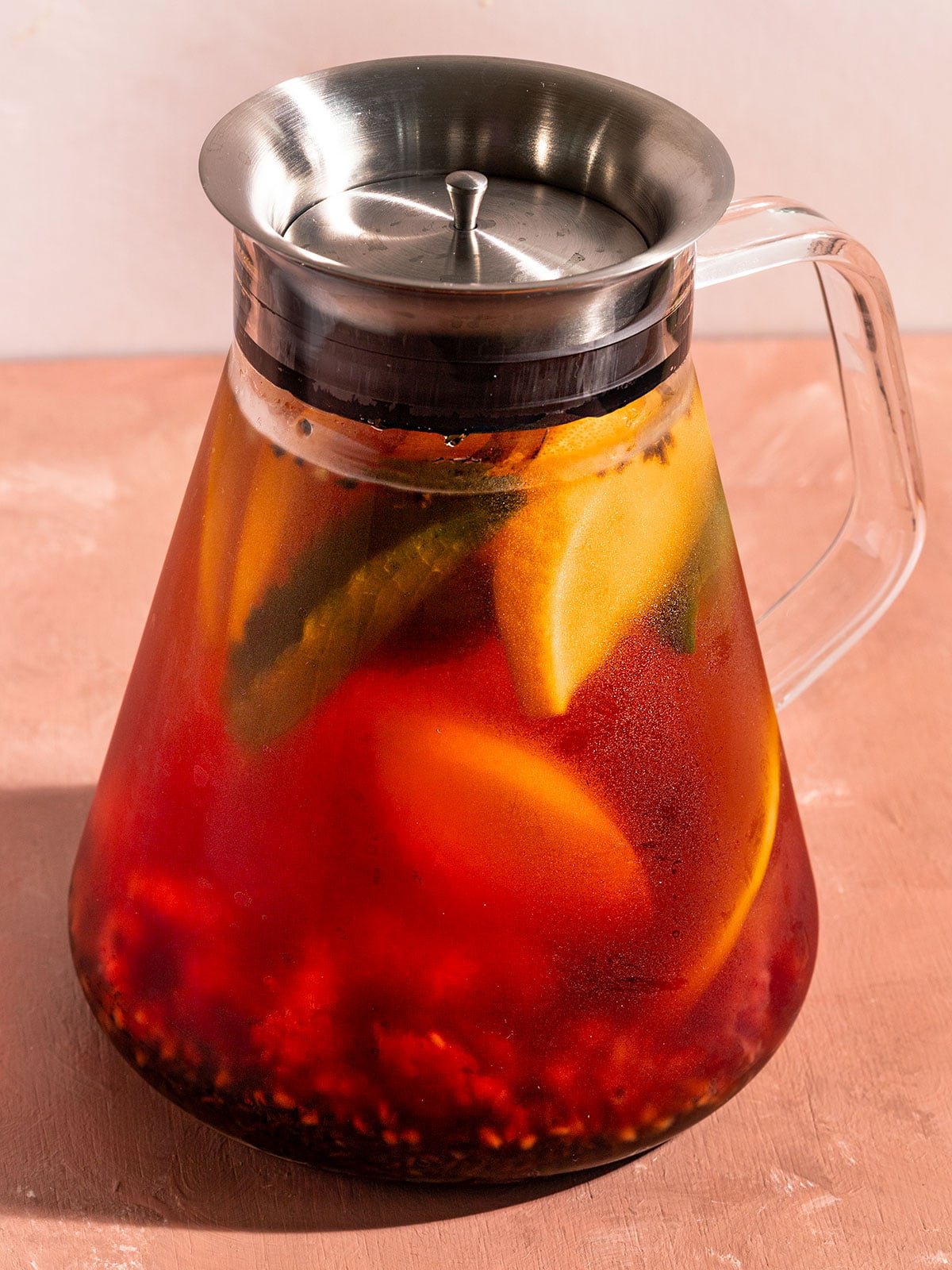 tea pot filled with brewed tea with water, muddled raspberries, black tea leaves, orange slices, and mint.
