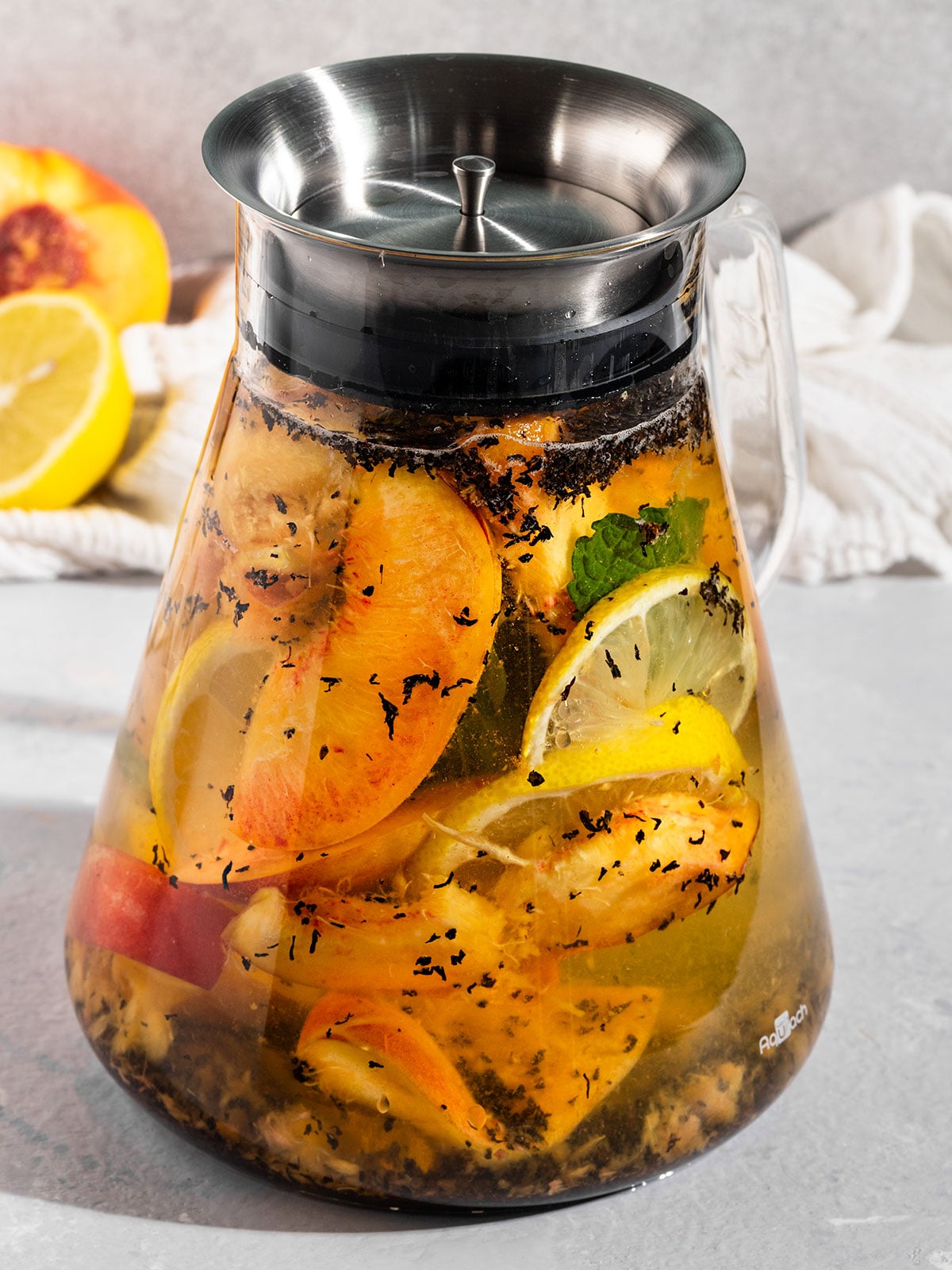 tea pot filled with water, peaches, mint, black tea leaves, and lemon.