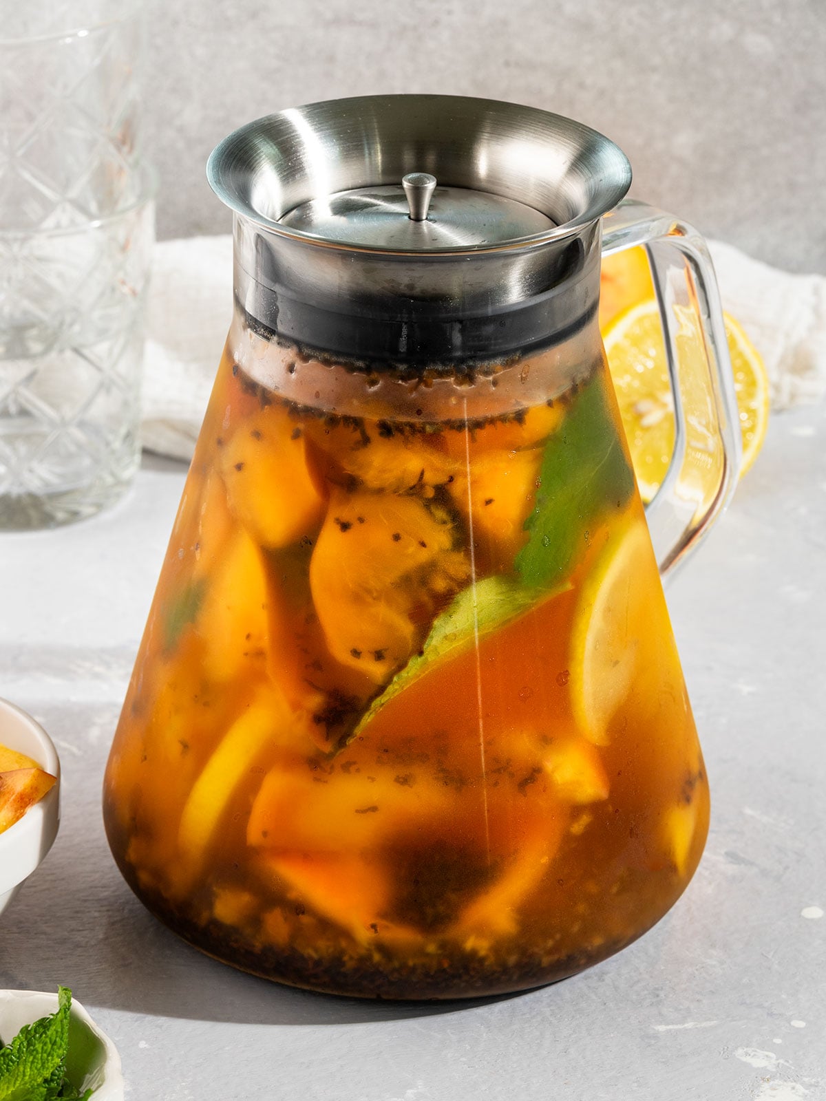 tea pot filled with water, peaches, mint, black tea leaves, and lemon.
