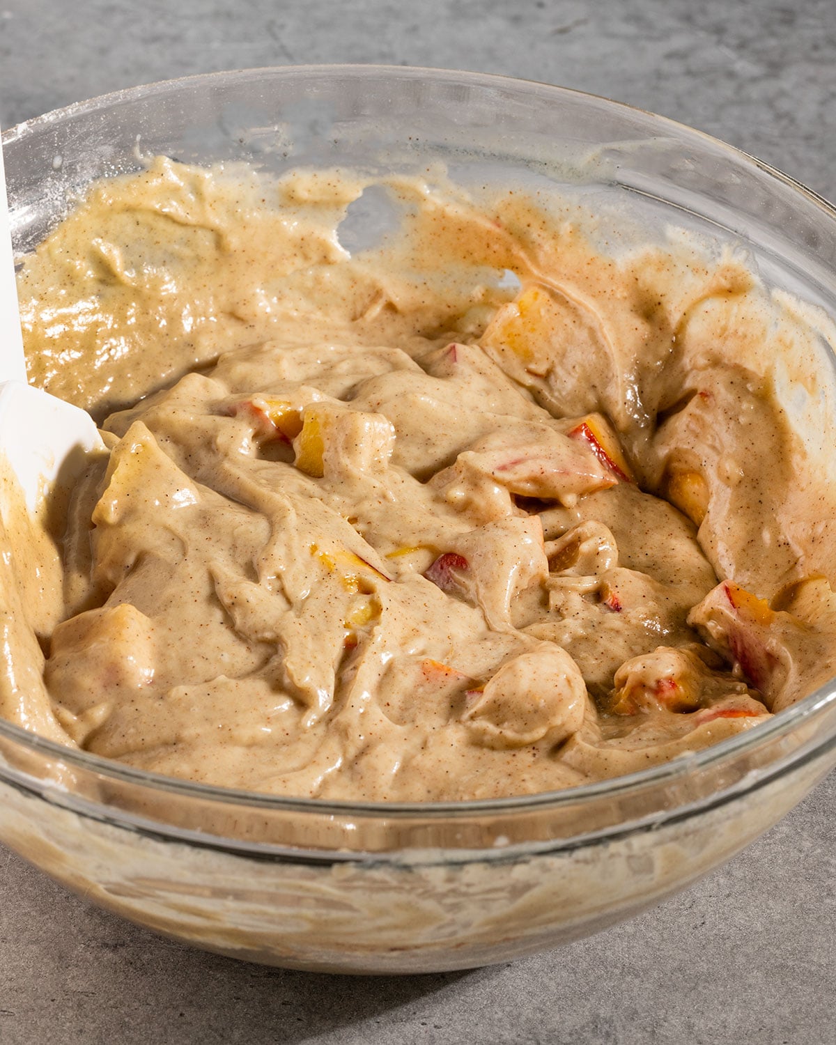 bowl of cinnamon cake batter with fresh peaches mixed in and a spatula.