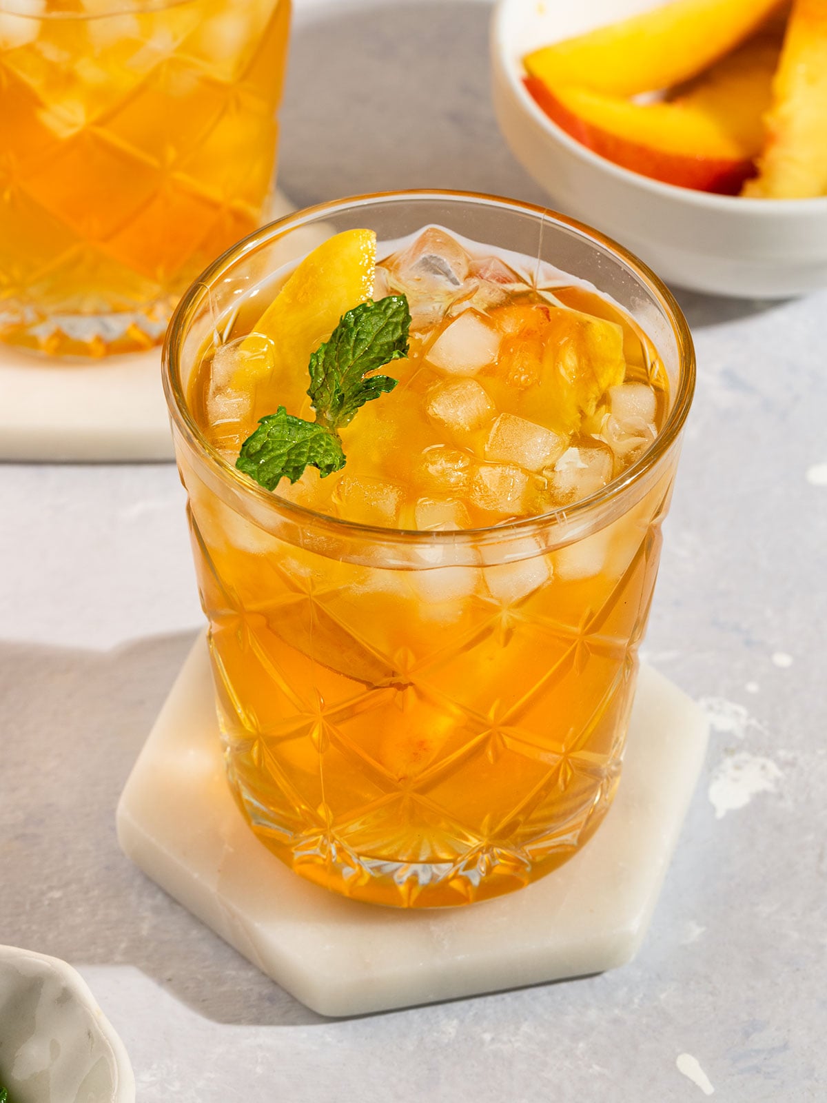 two glasses of peach tea filled with ice, fresh peach slices, and topped with sprig of mint.