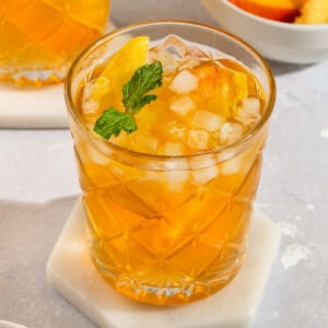 glass of peach tea filled with ice, fresh peach slices, and topped with sprig of mint.