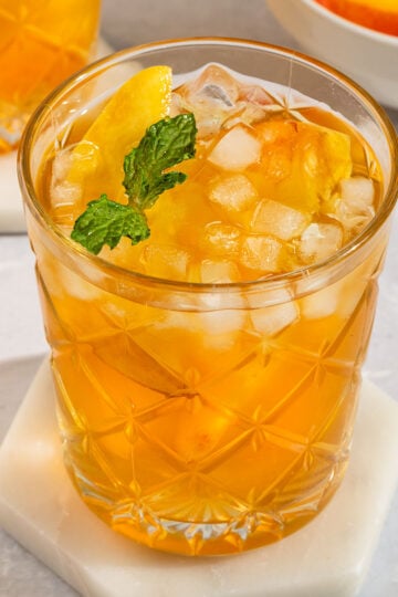 glass of peach tea filled with ice, fresh peach slices, and topped with sprig of mint.
