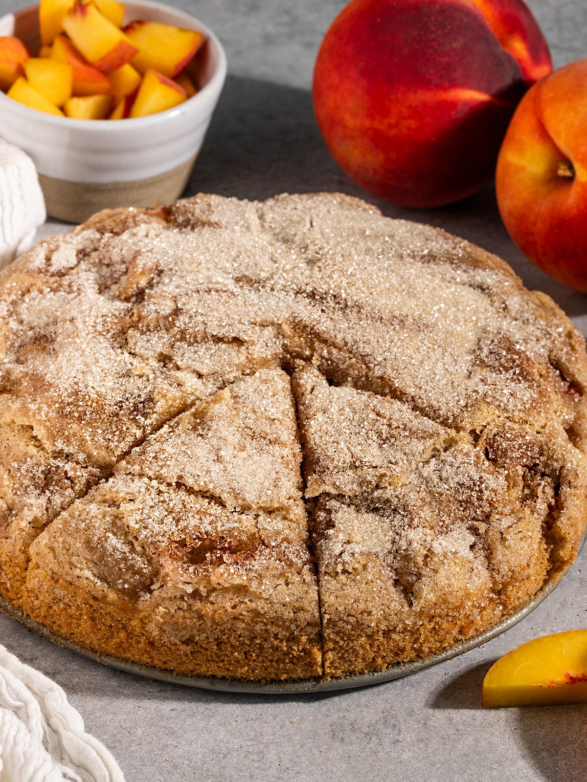 cake with sugar topping with two triangular slices cut out and fresh peaches on side.
