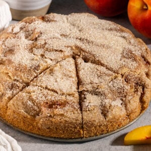 cake with sugar topping with two triangular slices cut out and fresh peaches on side.