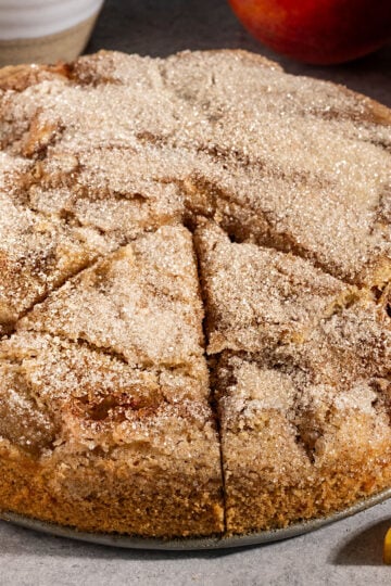 cake with sugar topping with two triangular slices cut out and fresh peaches on side.