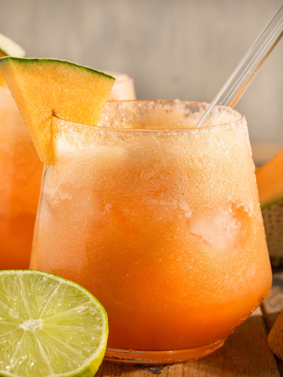 glass full of orange cantaloupe agua fresca with sparkling water and bubbles on top, a lime wedge, and a wedge of cantaloupe on the glass.