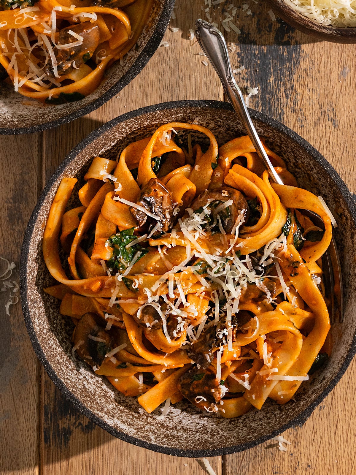 bowl of fettuccine with a red tomato sauce, mushrooms, spinach, and shredded parmesan cheese on top with fork in the bowl.