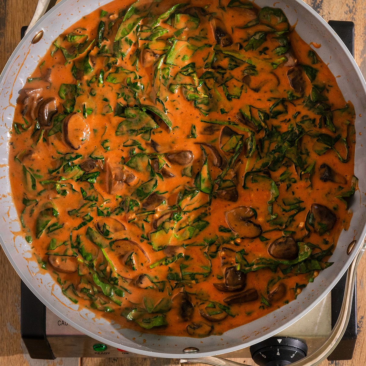 pan filled with a creamy red tomato sauce, cooked mushrooms, and cooked spinach.