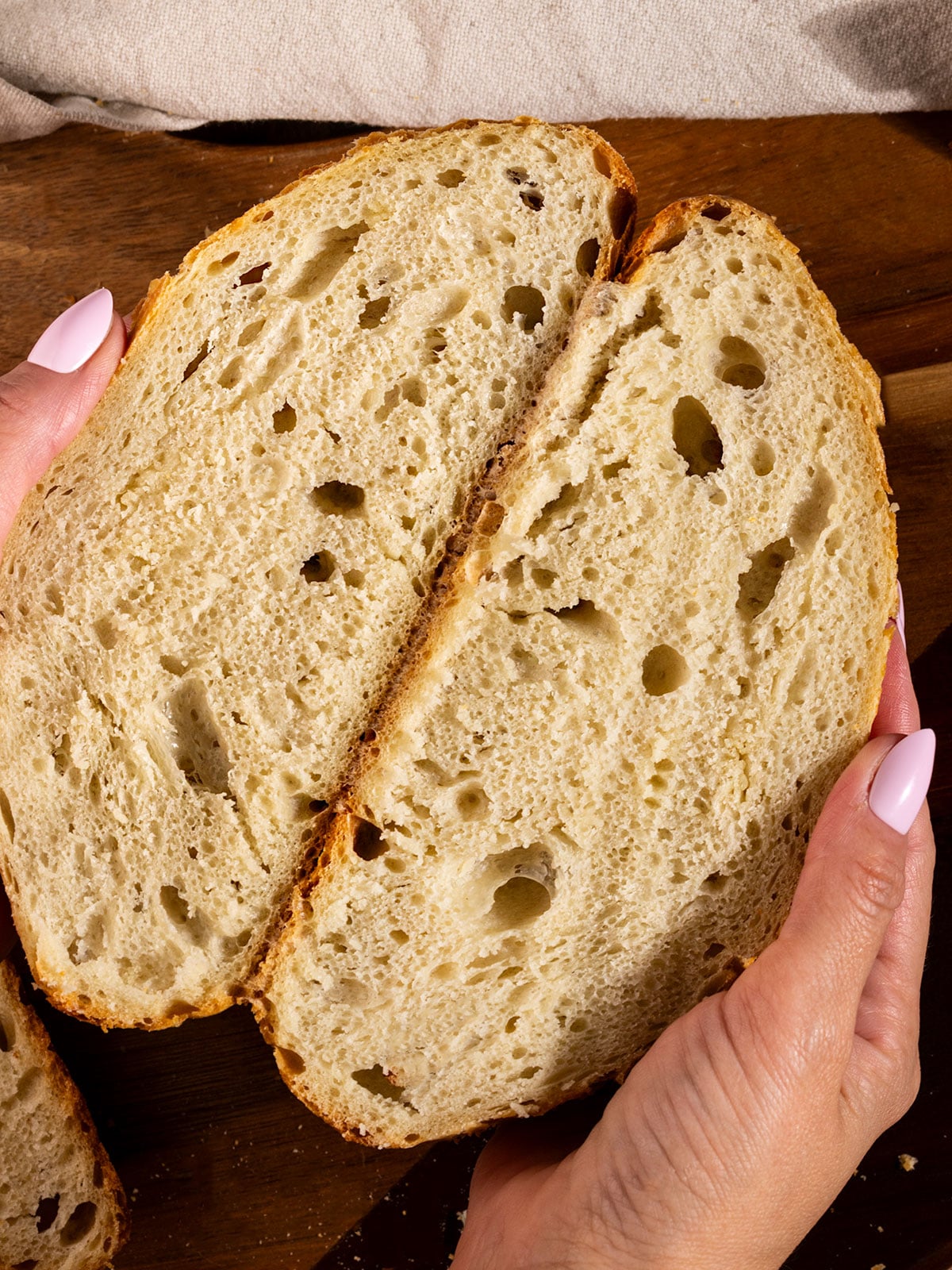 hands holding a loaf oc bread cut in half to show soft interior with air bubbles.