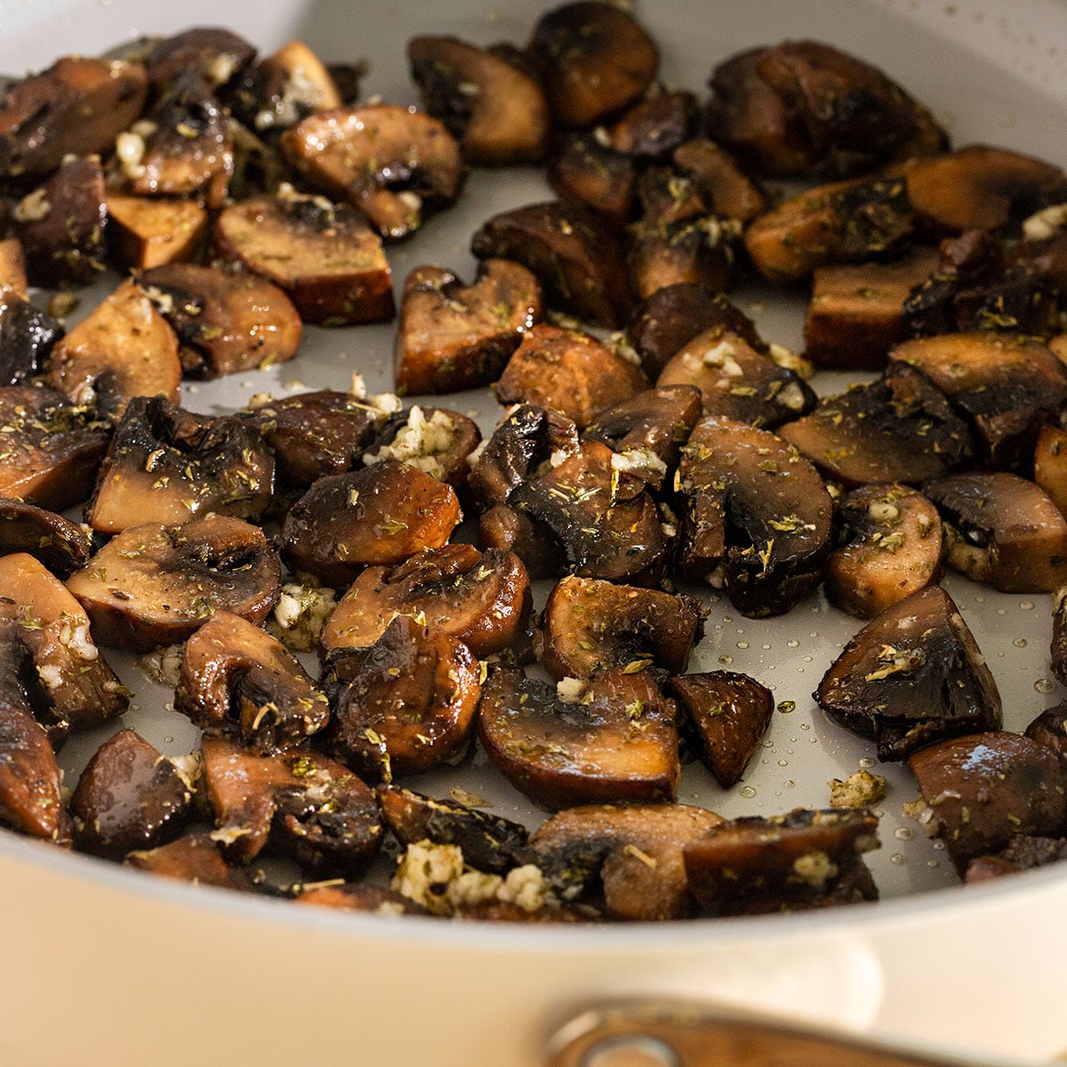 saute pan filled with browned sliced mushrooms and minced garlic cooking.