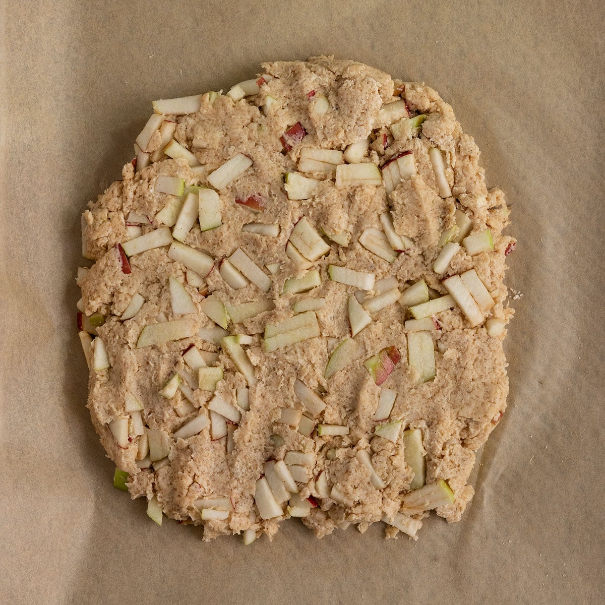 parchment lined tray topped with apple scone dough shaped into a round disc.