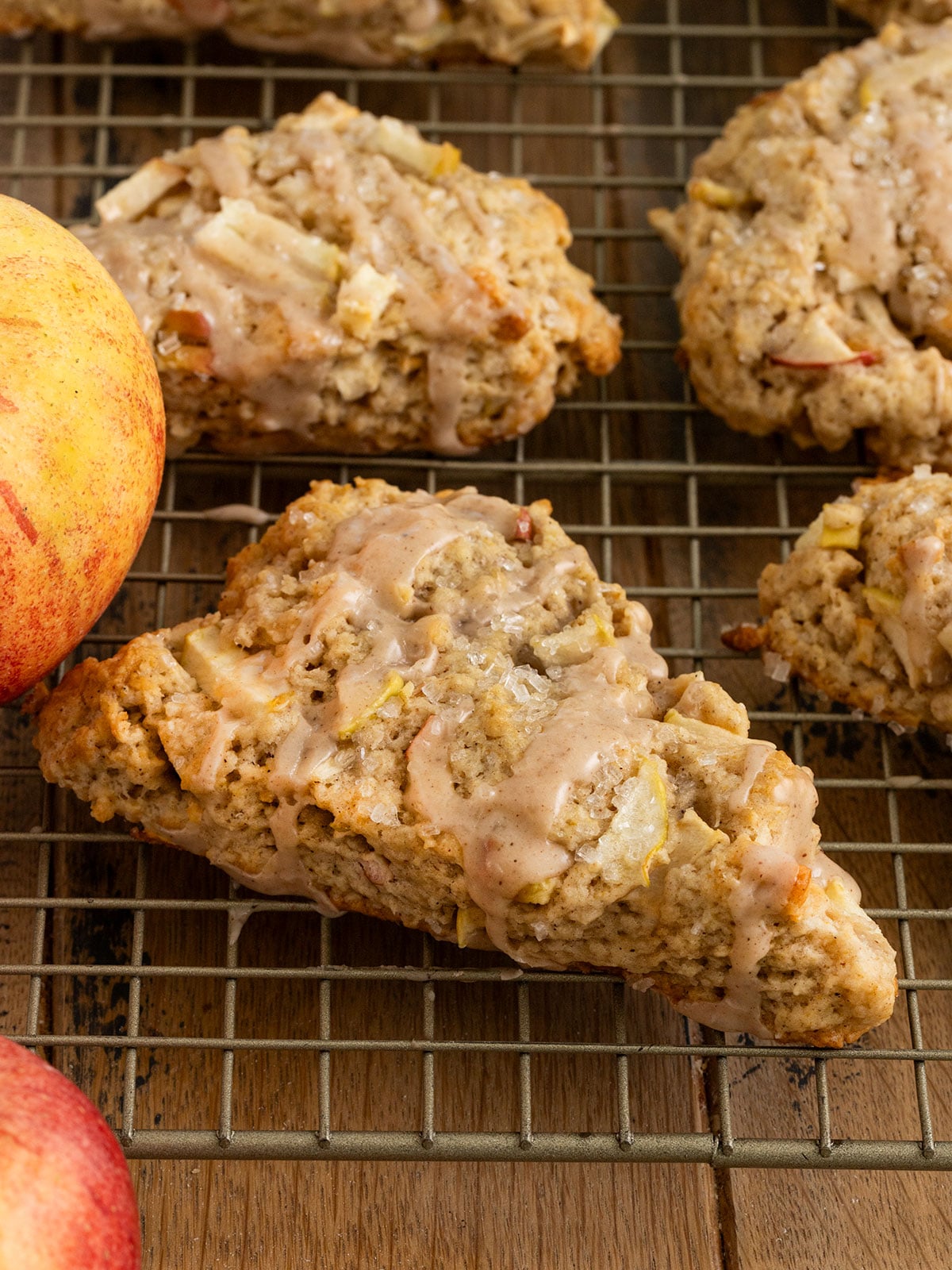 metal drying rack topped with several triangle scones filled with chunks of apples and topped with sparkling sugar and an apple spice icing.