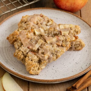 plate with two scones on top of each other filled with chunks of apples and topped with sparkling sugar and an apple spice icing.