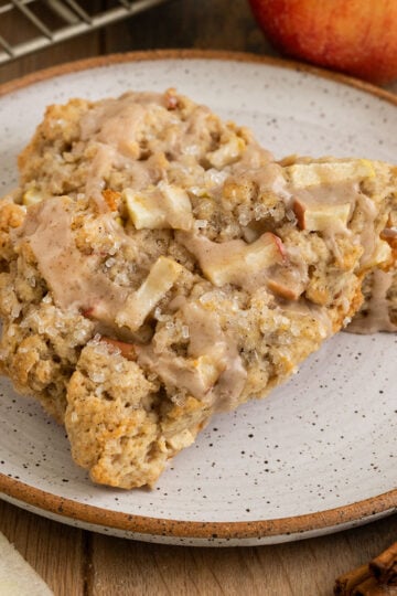 plate with two scones on top of each other filled with chunks of apples and topped with sparkling sugar and an apple spice icing.
