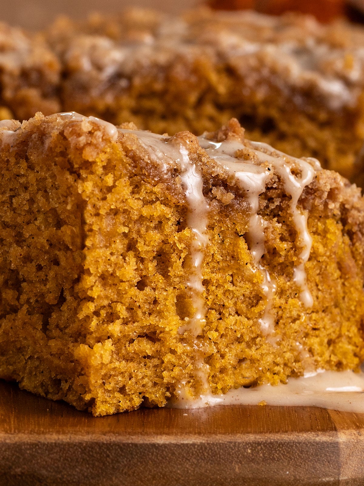 close up shot of a slice of pumpkin cake topped with streusel topping and a drizzle of pumpkin spice icing.