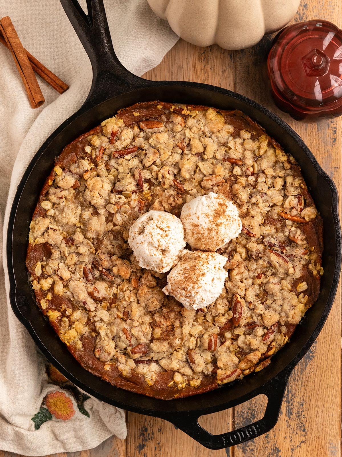 cast iron skillet filled with pumpkin filling, streusel topping, and 2 scoops of ice cream alongside mini pumpkins.
