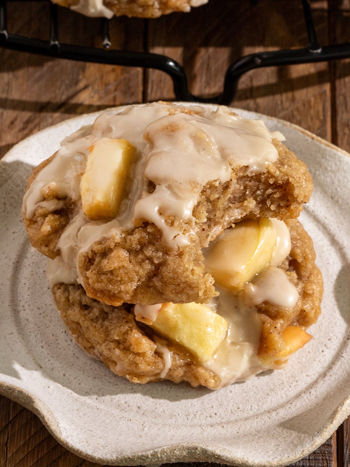 two cookies stacked onto plate filled with apples and topped with maple icing where top cookie has a bite taken out.