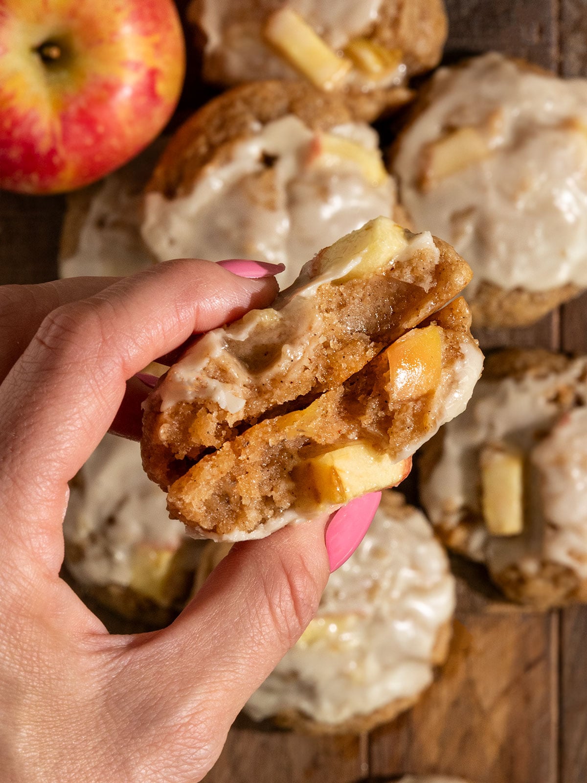 hand holding up a cookie broken in half with chunks of apples inside.