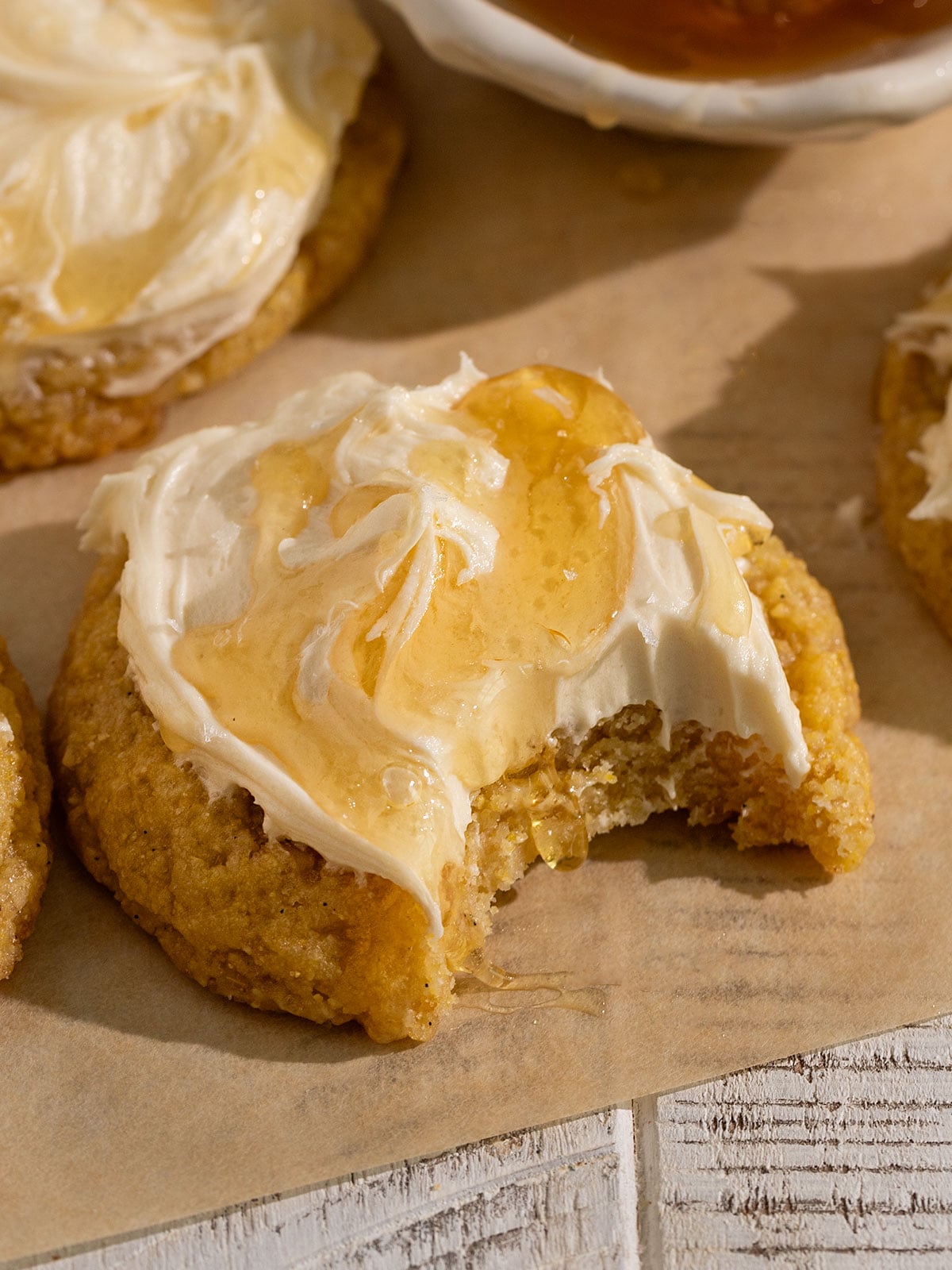 yellow cornbread cookie topped with frosting, honey, and flaky sea salt with a bite taken out.